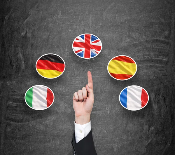 Concepto de proceso de estudio de lenguas extranjeras. Un dedo señala la bandera del Reino Unido como una prioridad en la elección de idiomas extranjeros. Fondo de pizarra negro . — Foto de Stock