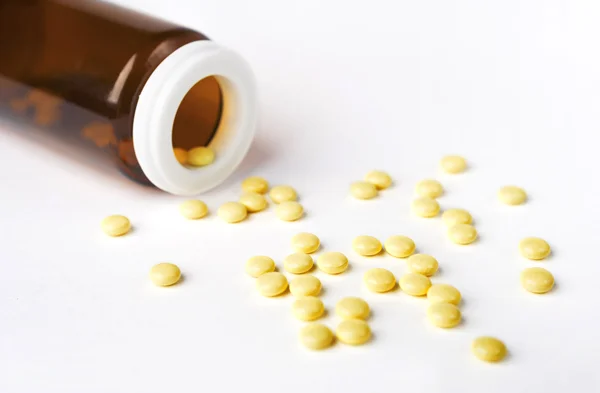 Żółte tabletki rozlane z butelki na białej powierzchni — Zdjęcie stockowe