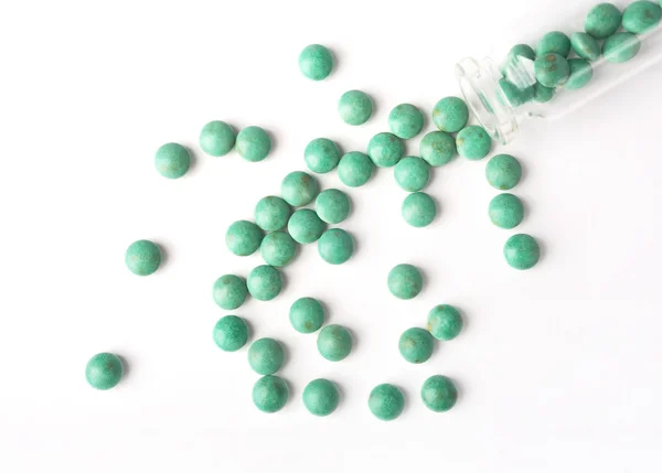 Vista dall'alto delle pillole verdi che vengono versate da una bottiglia sulla superficie bianca — Foto Stock