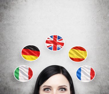 A concept of foreign language studying process. A foreseen of the brunette girl surrounded by icons of european flags. Concrete background.