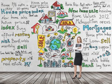 Full length beautiful woman in formal clothes holds a black folder. Colourful 'home sales' icons are drawn on the concrete wall. Risk analysis of the mortgage loan. Wooden floor.