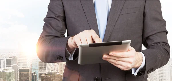 A man in formal suit is looking for some data in the tablet. Panorama of New York city on the background. — Stock Photo, Image