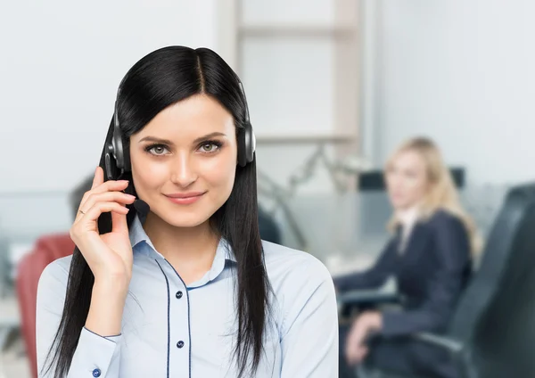 Vista frontale del sorridente operatore telefonico di supporto bruna con auricolare. Ufficio sfondo sul posto di lavoro in sfocatura . — Foto Stock