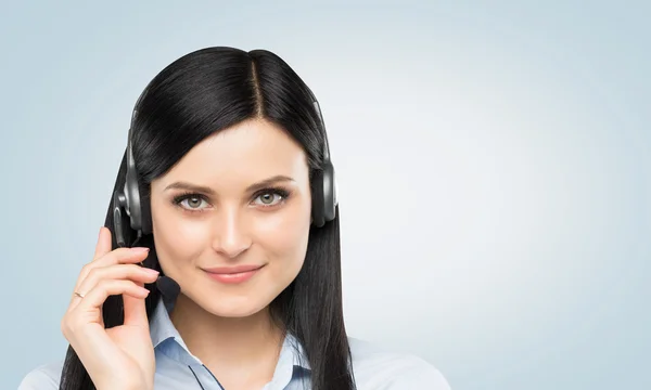 Front view of the smiling brunette support phone operator with headset. Light blue background. — Stock Photo, Image