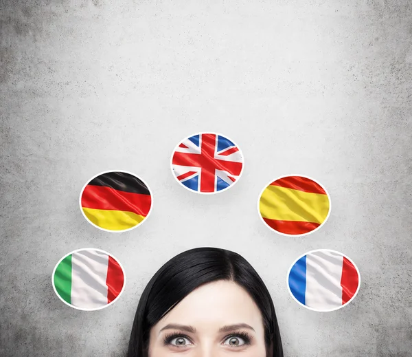 Concepto de proceso de estudio de lenguas extranjeras. Un previsto de la chica morena rodeada de iconos de banderas europeas. Fondo de hormigón . —  Fotos de Stock