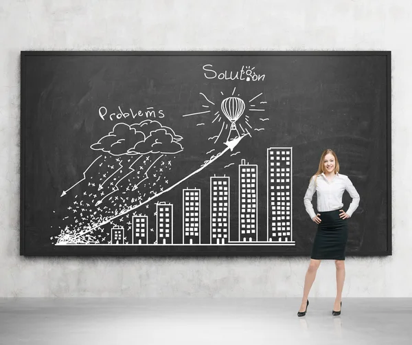 A brunette young woman in formal clothes holds her hands on the waist. Young professional presents ' Problems and solution ' strategy with the graph on the black chalkboard. Concrete room. — 스톡 사진