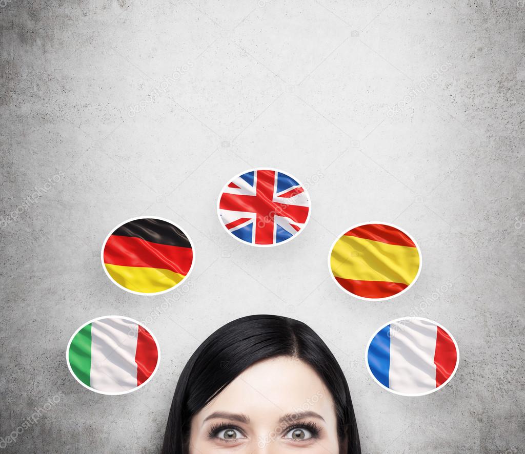 A concept of foreign language studying process. A foreseen of the brunette girl surrounded by icons of european flags. Concrete background.