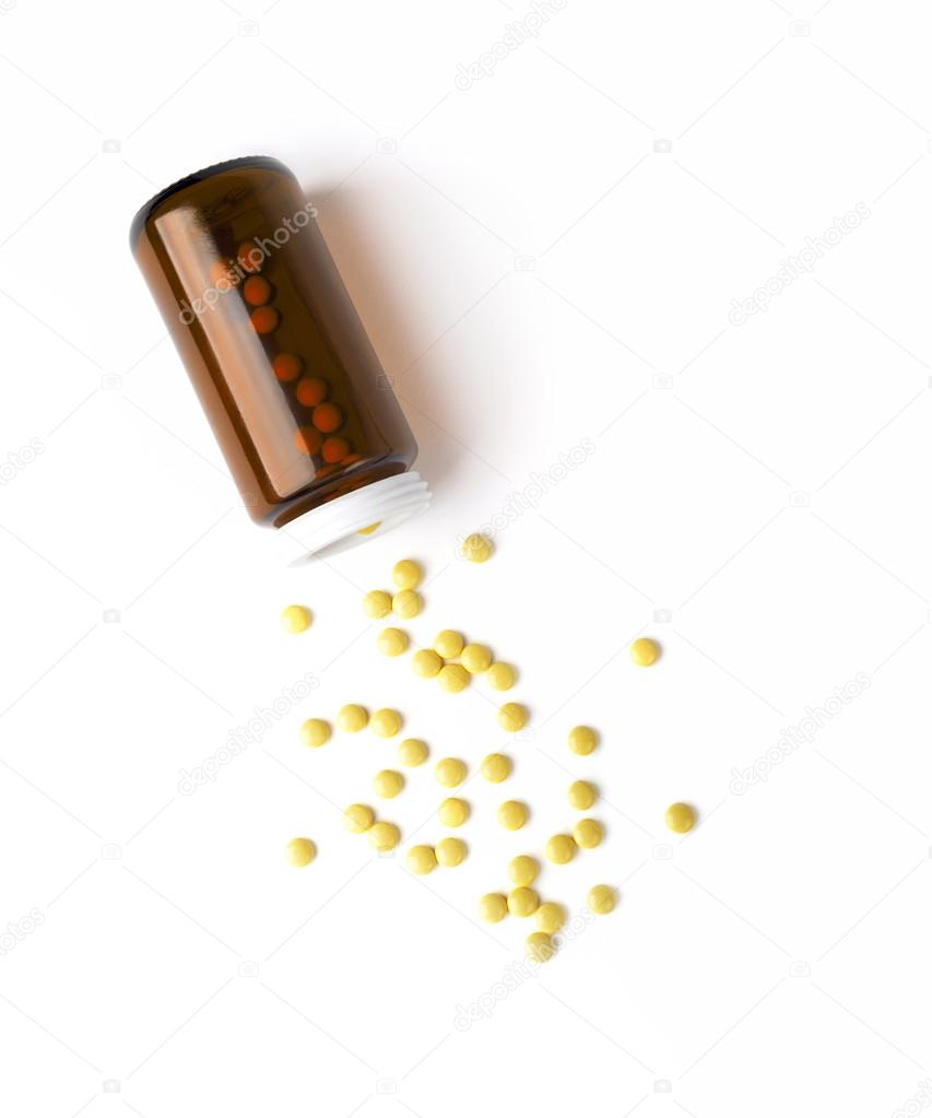 Top view of the spilled yellow pills from the medicine glass bottle. White surface.