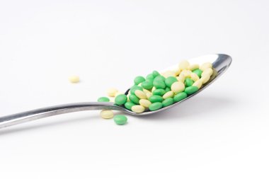 Sarı ve yeşil tıp hapları bir kaşık içinde bir yığın bir yan görünüm. Beyaz arka plan.