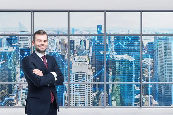 Smiling handsome businessman with cross hands is standing in the modern panoramic office. Financial charts are drawn over panoramic windows. New York cityscape. Manhattan. — Stock Fotó