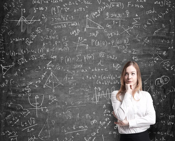 Bella signora in abiti formali pensando a possibili soluzioni dei problemi quantitativi. Le formule matematiche sono disegnate sulla lavagna nera . — Foto Stock
