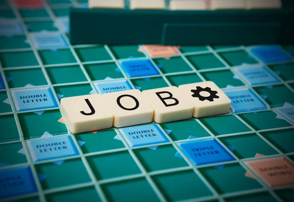 La palabra 'JOB' está hecha de las baldosas de scrabble. Scrabble tablero de juego como fondo . — Foto de Stock