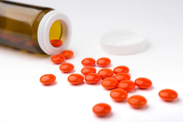 Le pillole versate arancioni da una bottiglia sono sulla superficie bianca . — Foto Stock