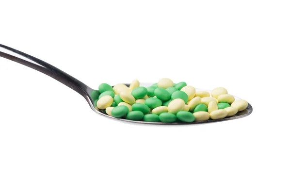 Eine Seitenansicht eines Haufens gelber und grüner Medikamententabletten in einem Löffel. isoliert auf weißem Hintergrund. — Stockfoto
