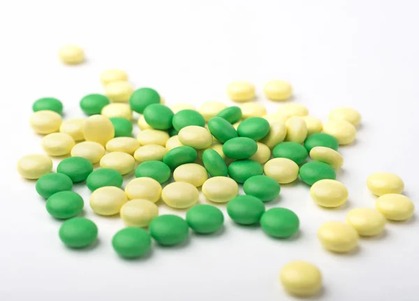 A heap of green and yellow medicine pills on white surface. — Stock Photo, Image