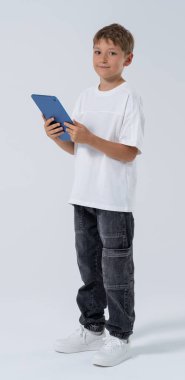 Young boy holding tablet, casual clothing style, isolated on light background. Concept of child technology use, learning, and digital education