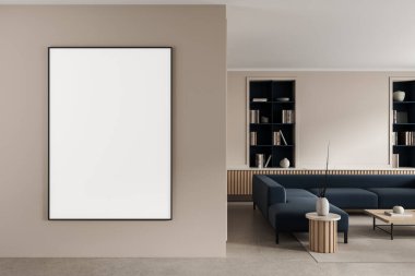 Blank vertical poster mockup on beige painted wall in modern living room with minimalist dark blue sofa, wooden tables, and bookshelves. 3D Rendering