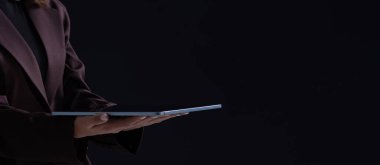 Kahverengi takım elbiseli, elinde parlak tablet, gerçekçi fotoğraf stili, koyu sade arka plan, teknoloji konsepti olan biri.