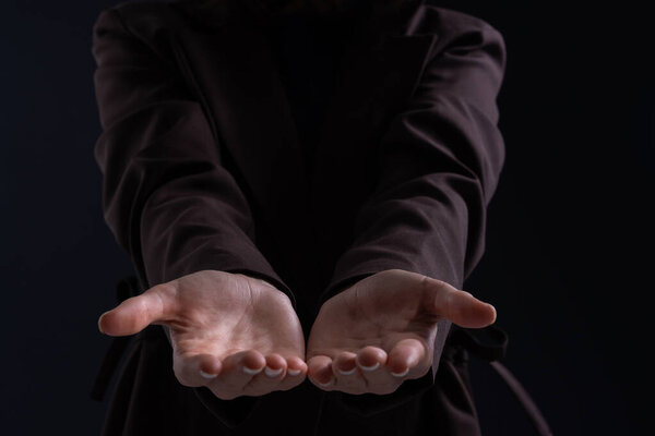 Женщина, протягивающая открытые руки вперед, одетая в темную одежду, низкосветлый студийный фон, концепция предложения, поддержка, уязвимость