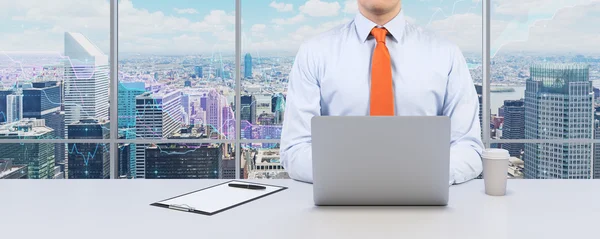 Молодой бизнесмен работает с ноутбуком. Современный панорамный офис или рабочее место с видом на город Нью-Йорк. Финансовая диаграмма за окнами . — стоковое фото