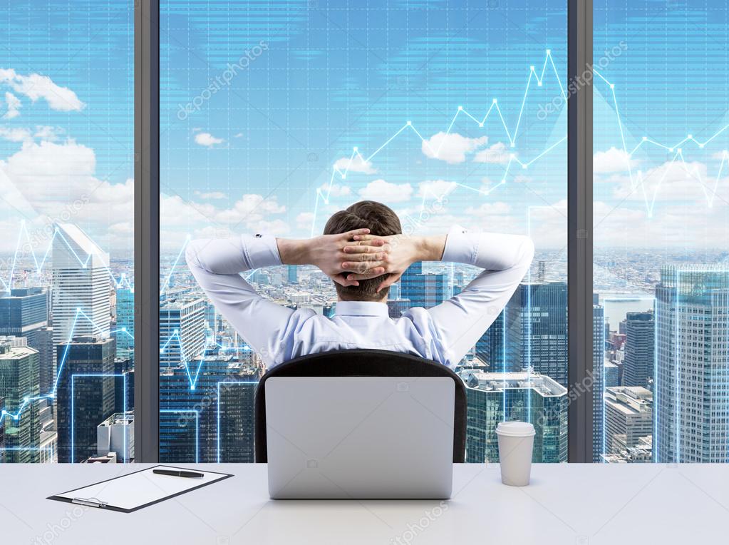 Rear view of the relaxing businessman with crossed hands behind his head, who is looking at NYC. Modern Panoramic office or work place with New York city view. Financial charts are over the windows.