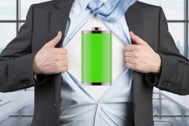 A man in a suit is tearing the blue shirt. Full charged battery on the chest. Modern panoramic office background.