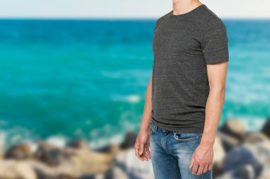 Side view of a man in a dark grey t-shirt and denims. Sea view background in blur.