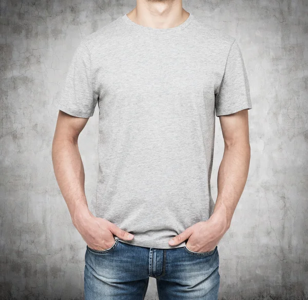 Un hombre con una camiseta gris y vaqueros sostiene sus manos en los bolsillos. Fondo de hormigón . —  Fotos de Stock