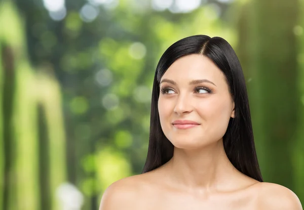 A portrait of a smiling brunette lady who is looking at something on the right side. Tropical landscape in blur on the background. — Stock Photo, Image