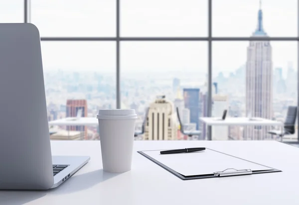 Un lugar de trabajo en una moderna oficina panorámica en Manhattan, Nueva York. Una computadora portátil, un bloc de notas y una taza de café están en la mesa blanca. Renderizado 3D . — Foto de Stock