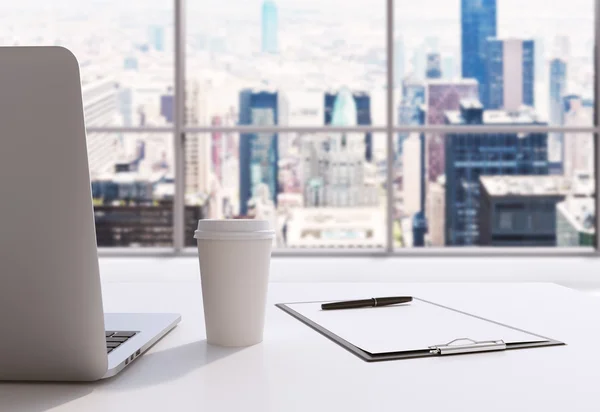 Um local de trabalho em um escritório panorâmico moderno em Manhattan, Nova York. Um laptop, um bloco de notas e uma xícara de café estão na mesa branca. Renderização 3D. Imagem tonificada . — Fotografia de Stock