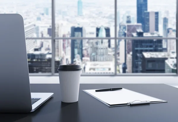 Un luogo di lavoro in un moderno ufficio panoramico a Manhattan, New York. Un computer portatile, un blocco note e una tazza di caffè sono sul tavolo nero. rendering 3D. Immagine tonica . — Foto Stock