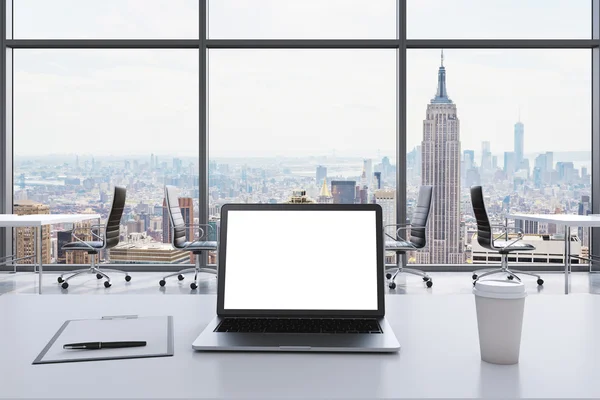 Un lieu de travail dans un bureau panoramique moderne à Manhattan, New York. Un ordinateur portable avec écran blanc, un bloc-notes et une tasse à café sont sur la table blanche. Chaises en cuir noir. Espace ouvert. rendu 3D . — Photo