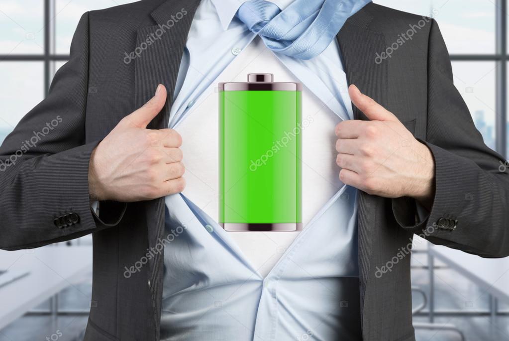 A man in a suit is tearing the blue shirt. Full charged battery on the chest. Modern panoramic office background.