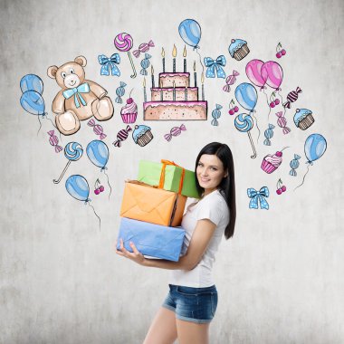 A brunette is holding three gift boxes. Birthday celebration colourful sketch is drawn on the concrete wall.