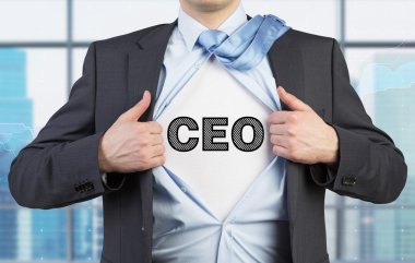 A man in a suit is tearing the blue shirt. Acronym CEO is drawn on the chest. Modern panoramic office background.