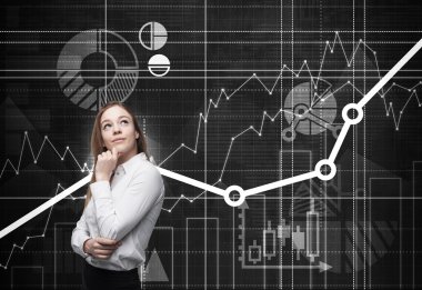 Beautiful young professional with the hand which holds her chin is thinking about future opportunities of the project. Financial analytic charts are drawn on the background.