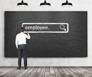 A handsome recruiter is writing down the word employee into the virtual searching bar in the black chalk board. The Internet concept of searching available candidates.
