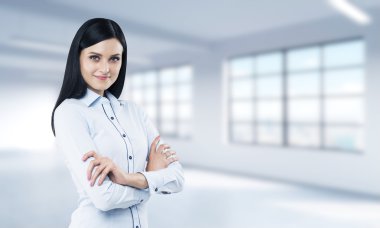 A brunette lady with crossed hands. Modern loft style open space as a background.