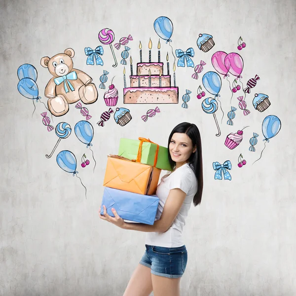 Una morena sostiene tres cajas de regalo. Celebración de cumpleaños dibujo colorido se dibuja en la pared de hormigón . — Foto de Stock