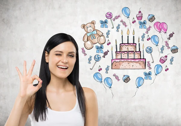 Брюнетка показує знак ОК. Барвистий торт на день народження намальований на бетонній стіні . — стокове фото