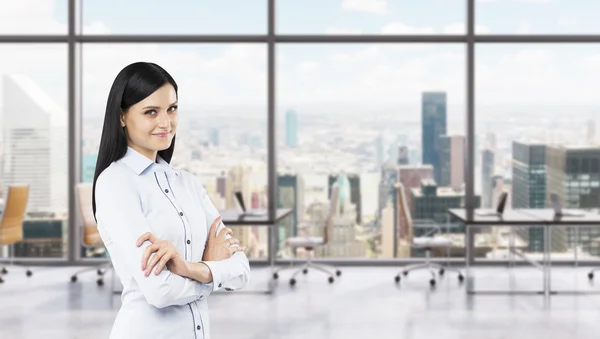 A side view of a beautiful smiling lady with crossed hands. The brunette woman is dressed in formal clothes. Modern workplaces in a fancy panoramic office in New York. — Stockfoto