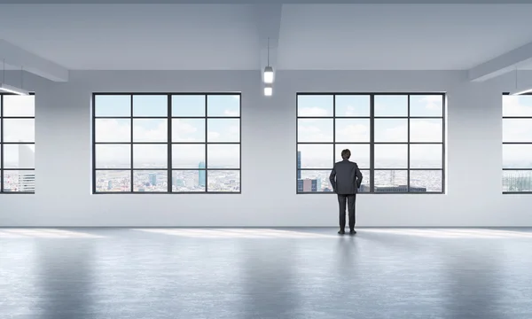 Full length a man in formal suit who is looking out the window in New York, modern loft style open space.