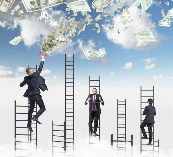 Confident handsome businessman on the ladder attracts dollar notes using a magnet. Sky with clouds on the background. — ストック写真