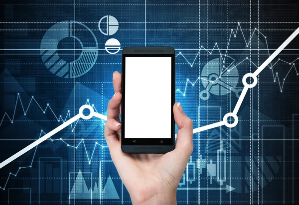 A hand holds a smartphone with white screen. Financial charts are drawn on the background — Stock Photo, Image