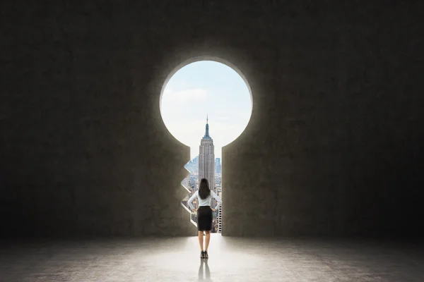 A keyhole in the concrete wall. A business lady dressed in formal suit is looking at New York City in the hole. There are drawn question marks around the hole. — ストック写真