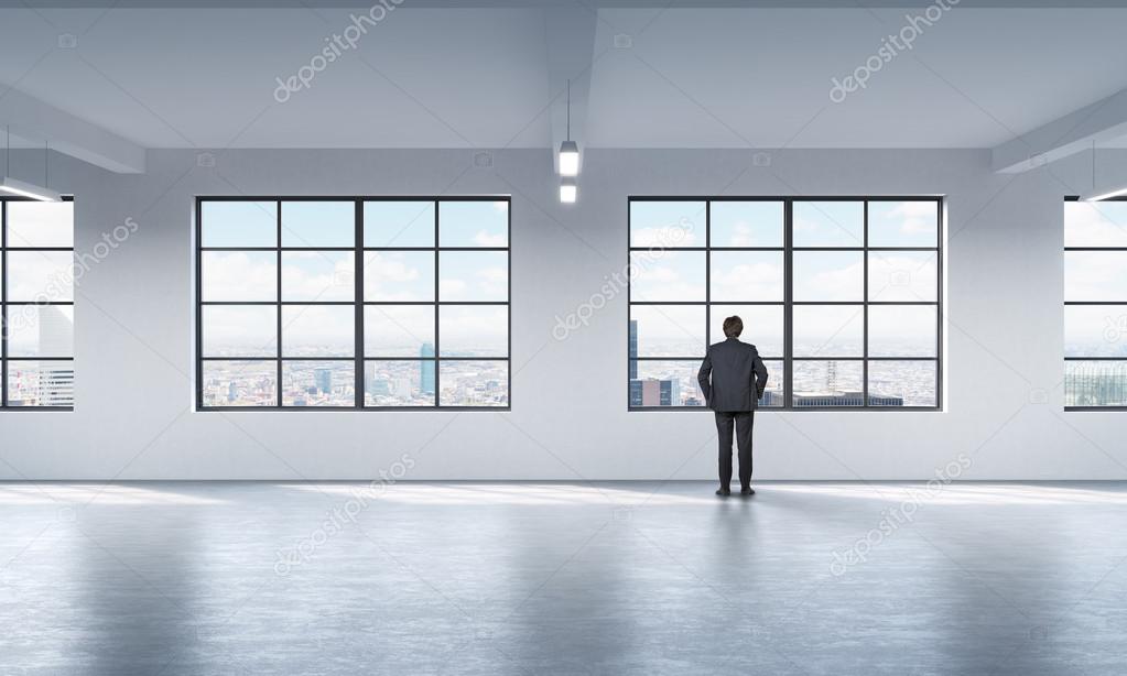 Full length a man in formal suit who is looking out the window in New York, modern loft style open space.