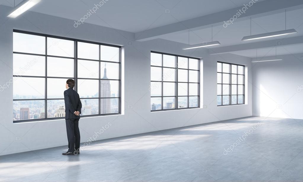 A full length man in formal suit who is looking out the window, New York panoramic view. A modern loft style open space.