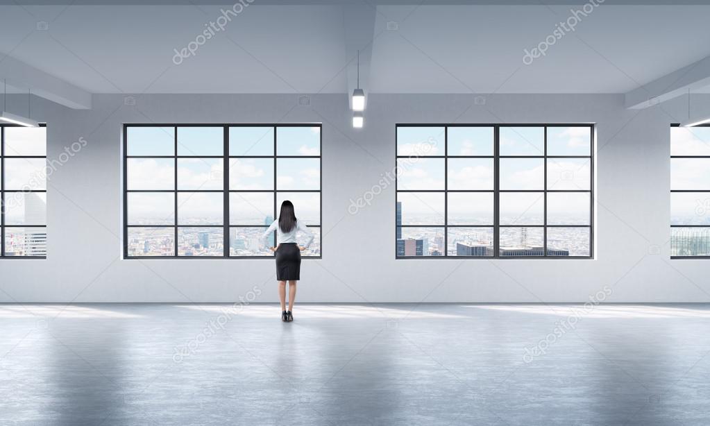 Rear view of a full length lady in formal clothes who is looking out the window in New York, modern loft style open space.