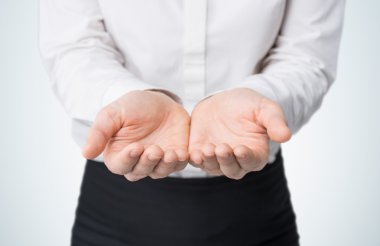 Close-up of woman's hands, palms up. A woman dressed in formal clothes. A light blue background.